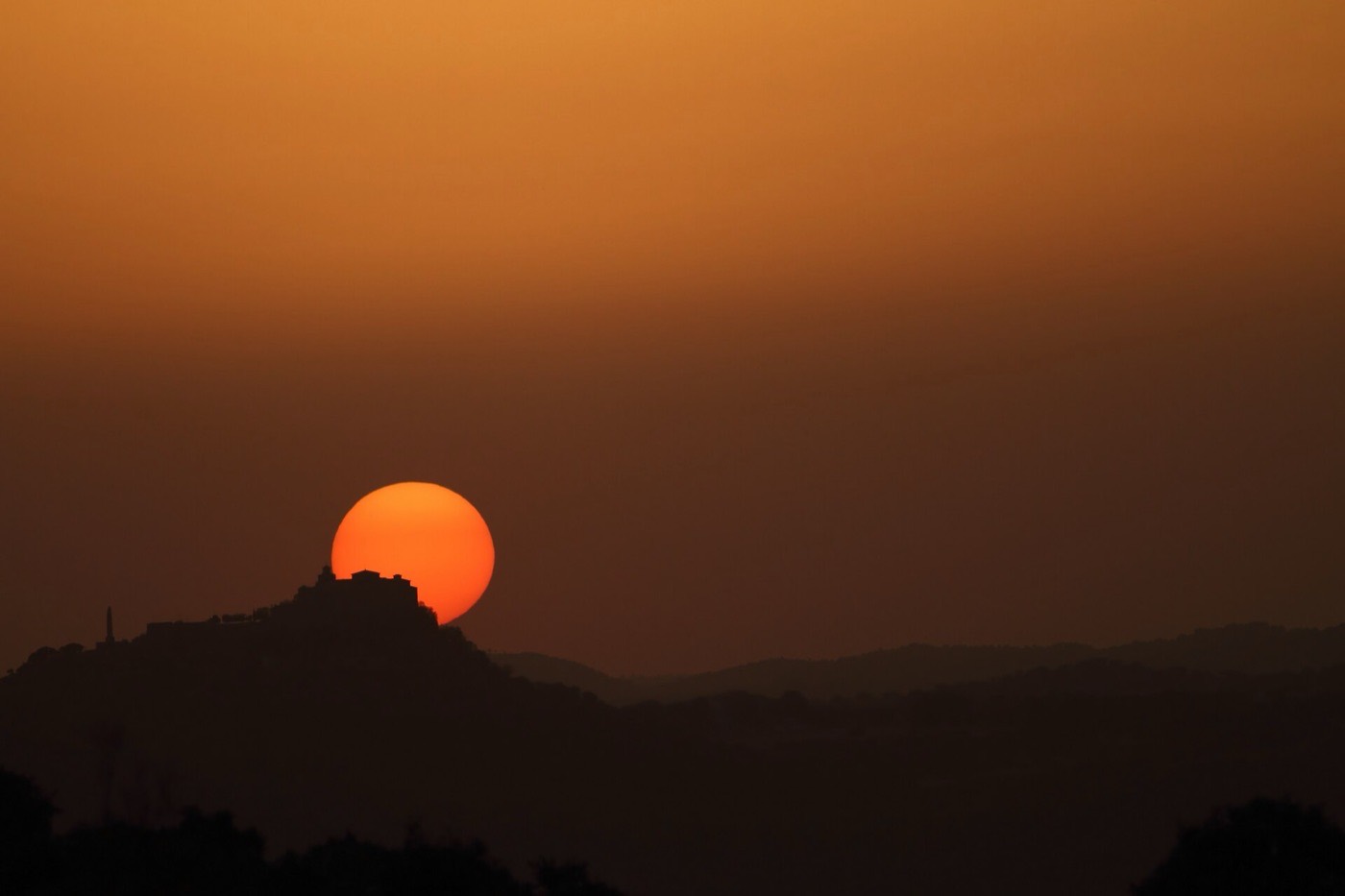 El Cerro del Cabezo con el Santuario recortado contra el sol del atardecer en la Sierra de Andújar.