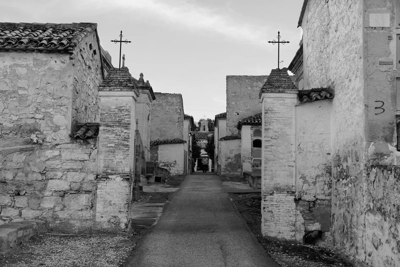 Calle entre bloques de nichos de piedra con cruces de hierro en el cementerio histórico de San Eufrasio de Jaén, en blanco y negro