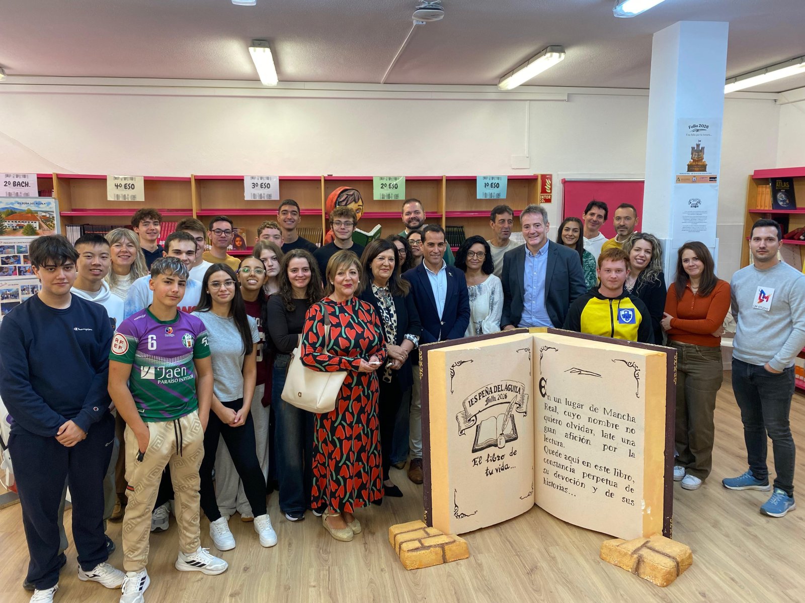 Un grupo de personas posa sonriente en una biblioteca junto a un gran libro decorativo abierto y estanterías con carteles de precios.