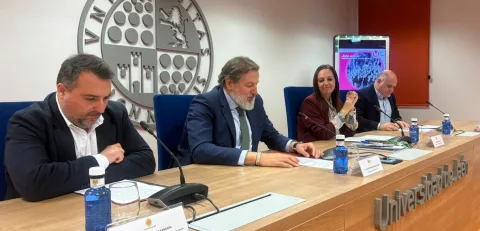Cuatro personas con traje sentadas tras una mesa con micrófonos y botellas de agua, ante un gran emblema circular en la pared.