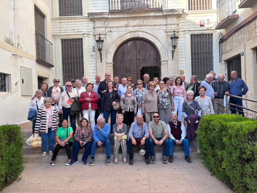 Un grupo numeroso de personas mayores posa en las escaleras de la entrada de un edificio con portón de madera.