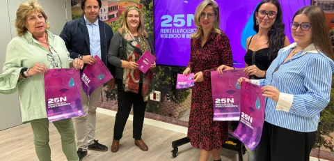 Seis personas de pie sostienen bolsas y folletos morados con el lema 25N ante un panel del mismo color.