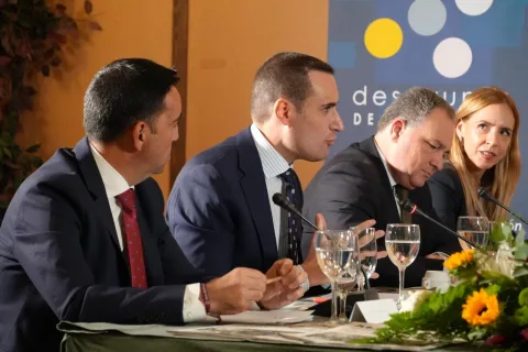 Cuatro personas con traje sentadas tras una mesa con micrófonos y vasos de agua, en una mesa redonda.