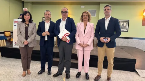 Cinco personas trajeadas posan en fila ante un escenario, con un cartel de encuentros sobre emprendimiento a la izquierda.