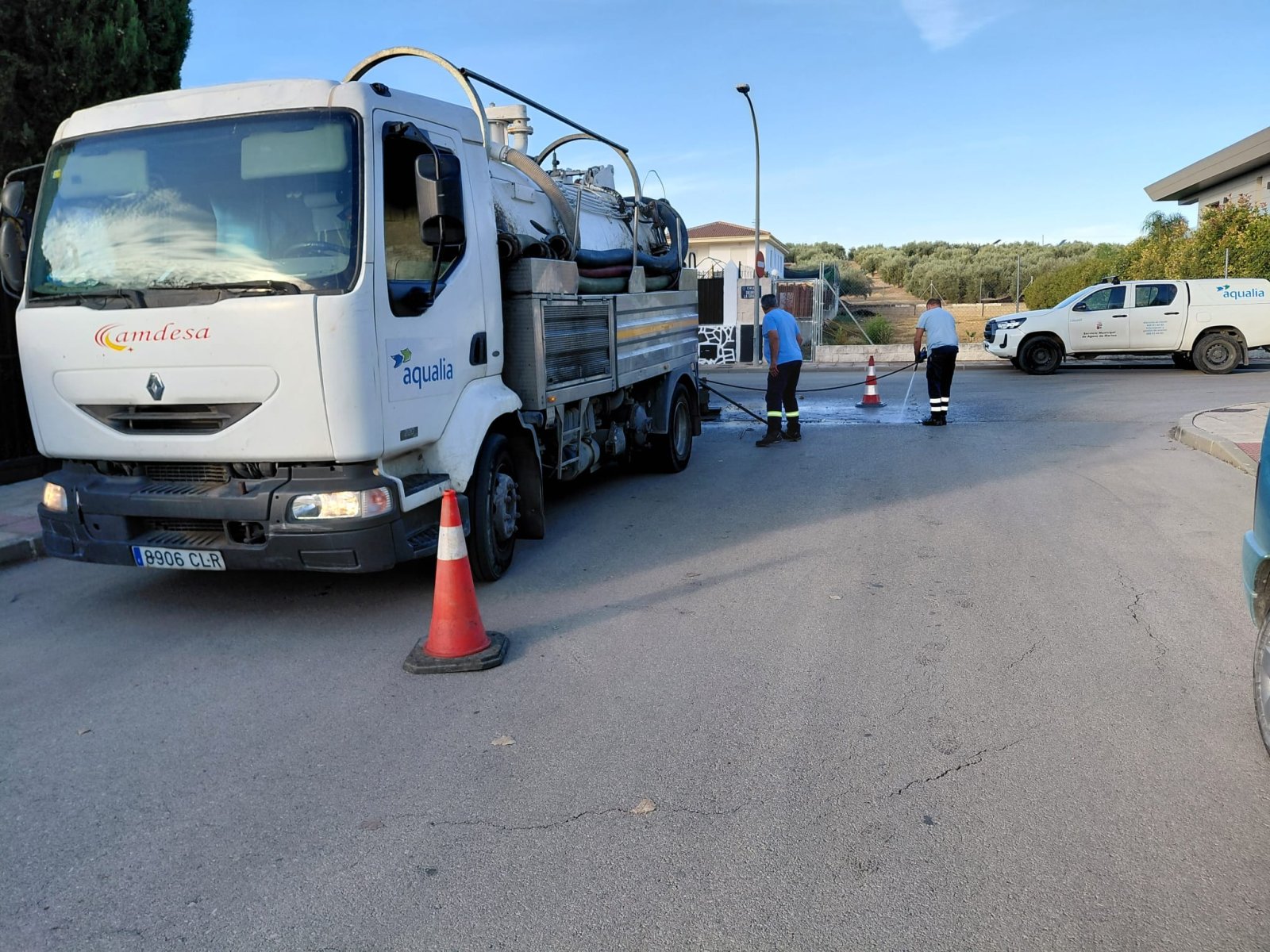 Un camión cisterna blanco con dos operarios manejando una manguera junto a conos en una calle.